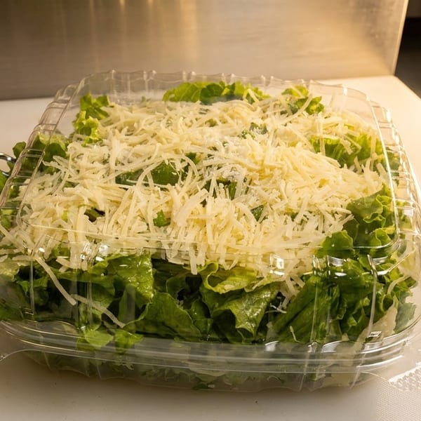 Fresh Caesar salad with shredded Parmesan cheese in a clear plastic to-go container.