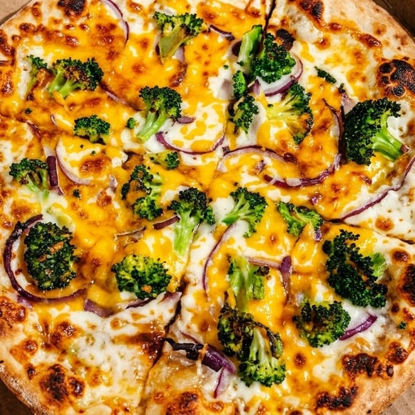 A whole pizza with broccoli, red onion, and melted cheese in a cardboard box.