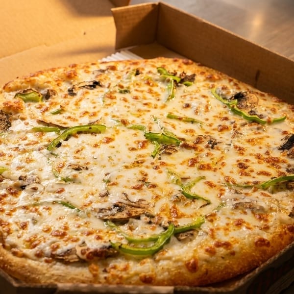 Freshly baked pizza with white sauce, mozzarella, mushrooms, and green peppers in a cardboard box.